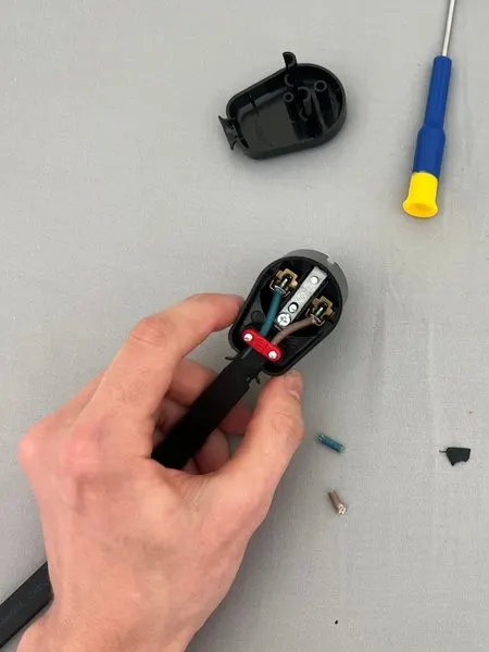My hand holding the open plug: a blue and a brown wire in the two outer terminals, under a red cord grip.